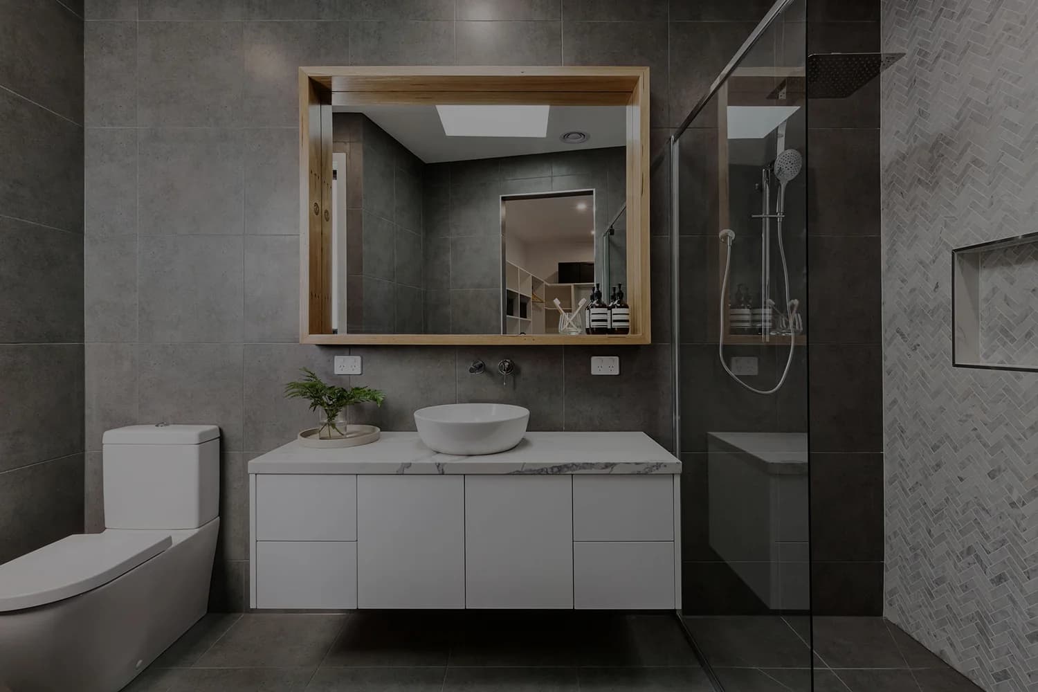 Renovated bathroom with grey stone tiling, timber framed mirror, vessel basin and walk-in shower